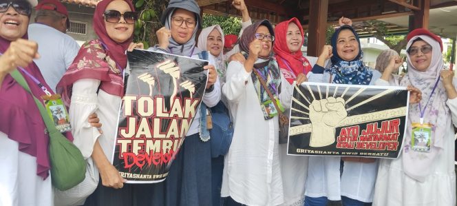 
 Berikut versi yang sudah dirapikan dan siap digunakan sebagai keterangan foto:
Para emak-emak warga Griya Shanta membawa poster berisi penolakan terhadap rencana pembongkaran tembok pembatas kawasan tersebut. (ist)