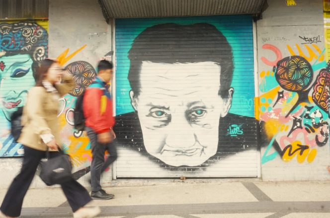 
 Pejalan kaki melintas mural Mbah Arifin atau Mbah Gombloh di Jalan Basuki Rahmad, Kayutangan Heritage Kota Malang. (Nedi Putra AW)
