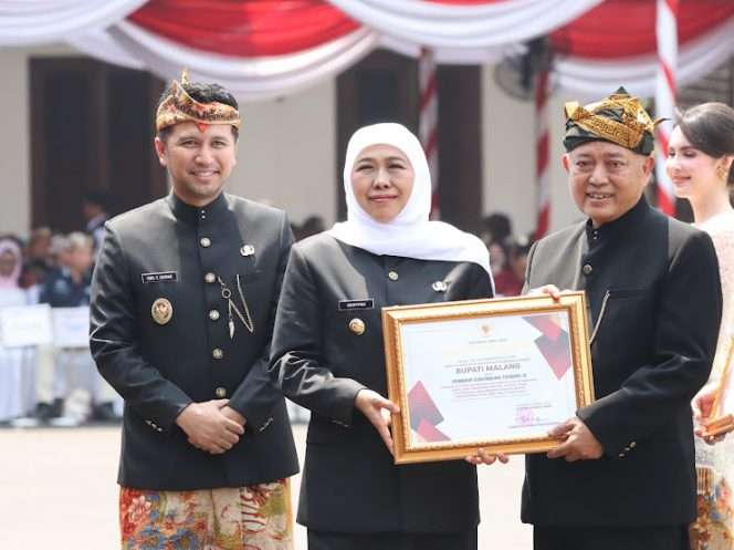 
 Berfoto bersama usai penyerahan penghargaan Juara Terbaik 3 Penilaian Sistem Keamanan Lingkungan (PIN) Siskamling Jogo Jawa Timur 2026 yang diraih Pemerintah Kabupaten Malang melalui RT 14 RW 11 Perumahan Banjararum Asri, Desa Banjararum, Kecamatan Singosari. Penghargaan diserahkan langsung oleh Gubernur Jawa Timur Khofifah Indar Parawansa kepada Bupati Malang Drs. H. M. Sanusi, M.M., dalam rangkaian Upacara Peringatan Hari Jadi ke-81 Provinsi Jawa Timur di Gedung Negara Grahadi, Surabaya, Senin (12/10/2026) pagi. (Humas Pemkab Malang)