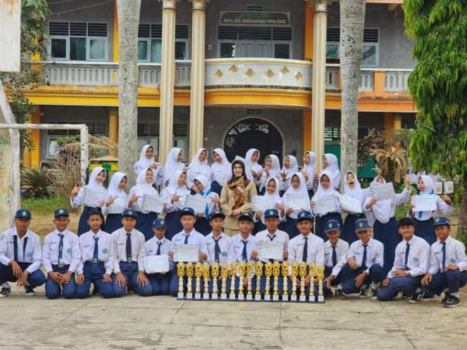 
 Kepala MTs Al-Hidayah Wajak Hernganti Ika Anggraina (tengah) berfoto bersama siswa, usai sekolahnya sukses meraih predikat juara umum Pekan Olahraga dan Seni (Porseni) tingkat Kelompok Kerja Madrasah (KKM) MTs An-Nur Bululawang tahun 2026. (Hernganti for bacamalang)