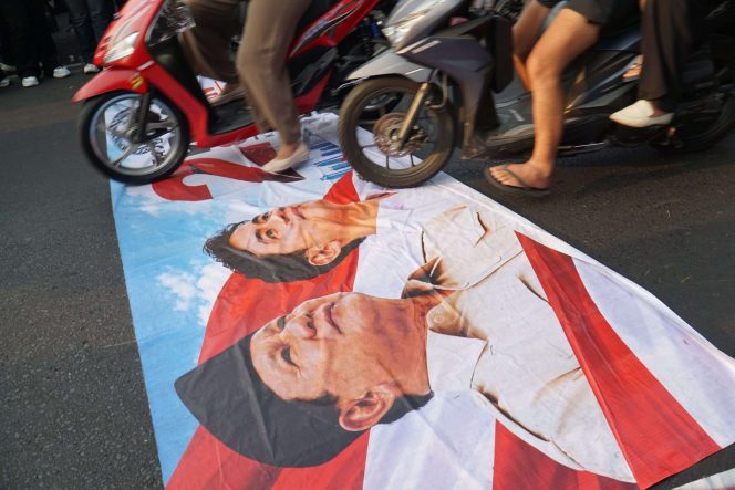
 Spanduk bertuliskan “2 Tahun Prabowo-Gibran” sempat dilindas kendaraan roda dua maupun roda empat yang melintas di tengah aksi unjuk rasa Aliansi Rakyat Bangkit Bersatu di sekitar Gedung DPRD Kota Malang, Jalan Tugu, Rabu (21/10/2026). (Nedi Putra AW).